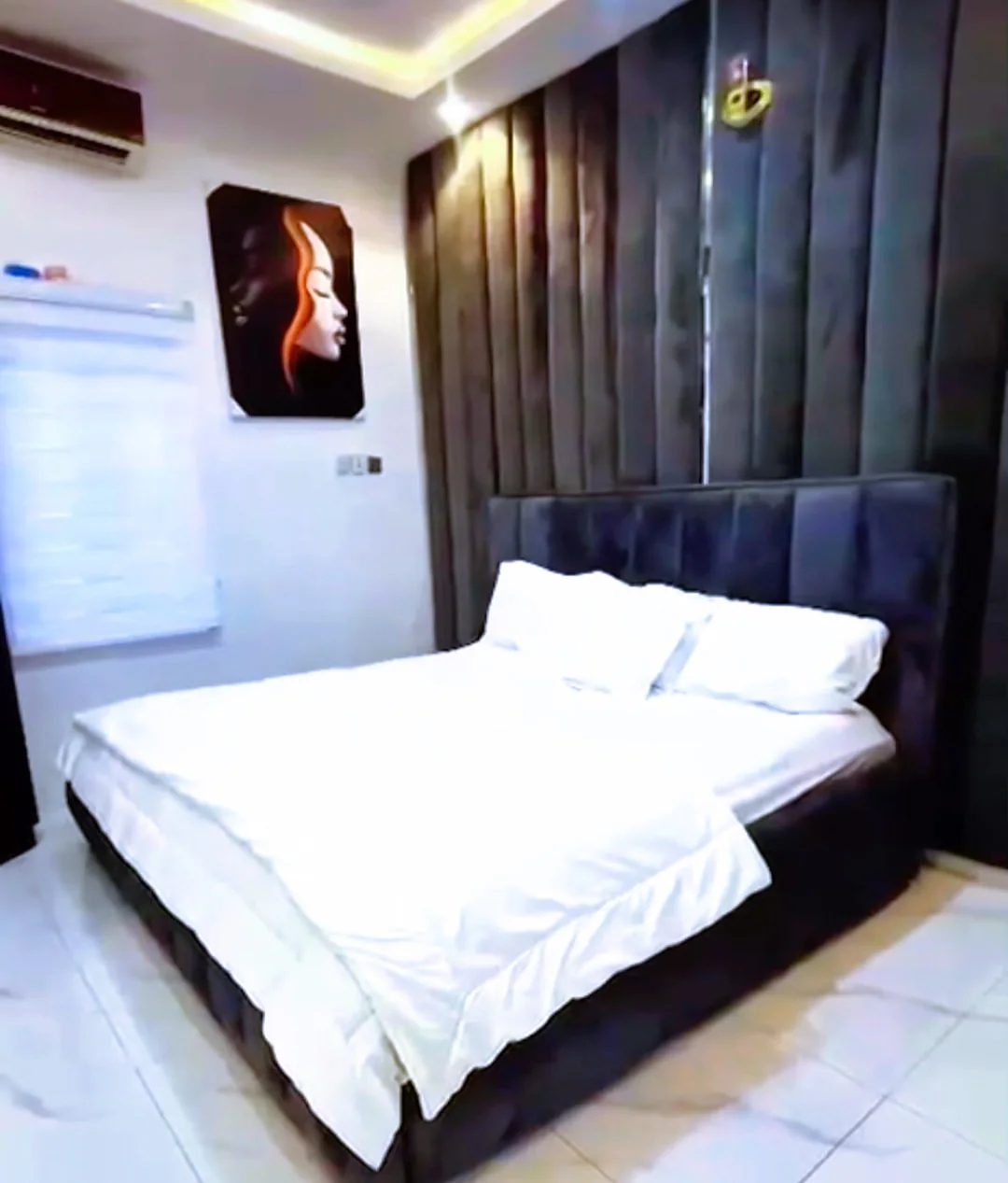 Laimon Apartment bedroom, with a dark framed bed dressed in white linen against fluted wall panelling